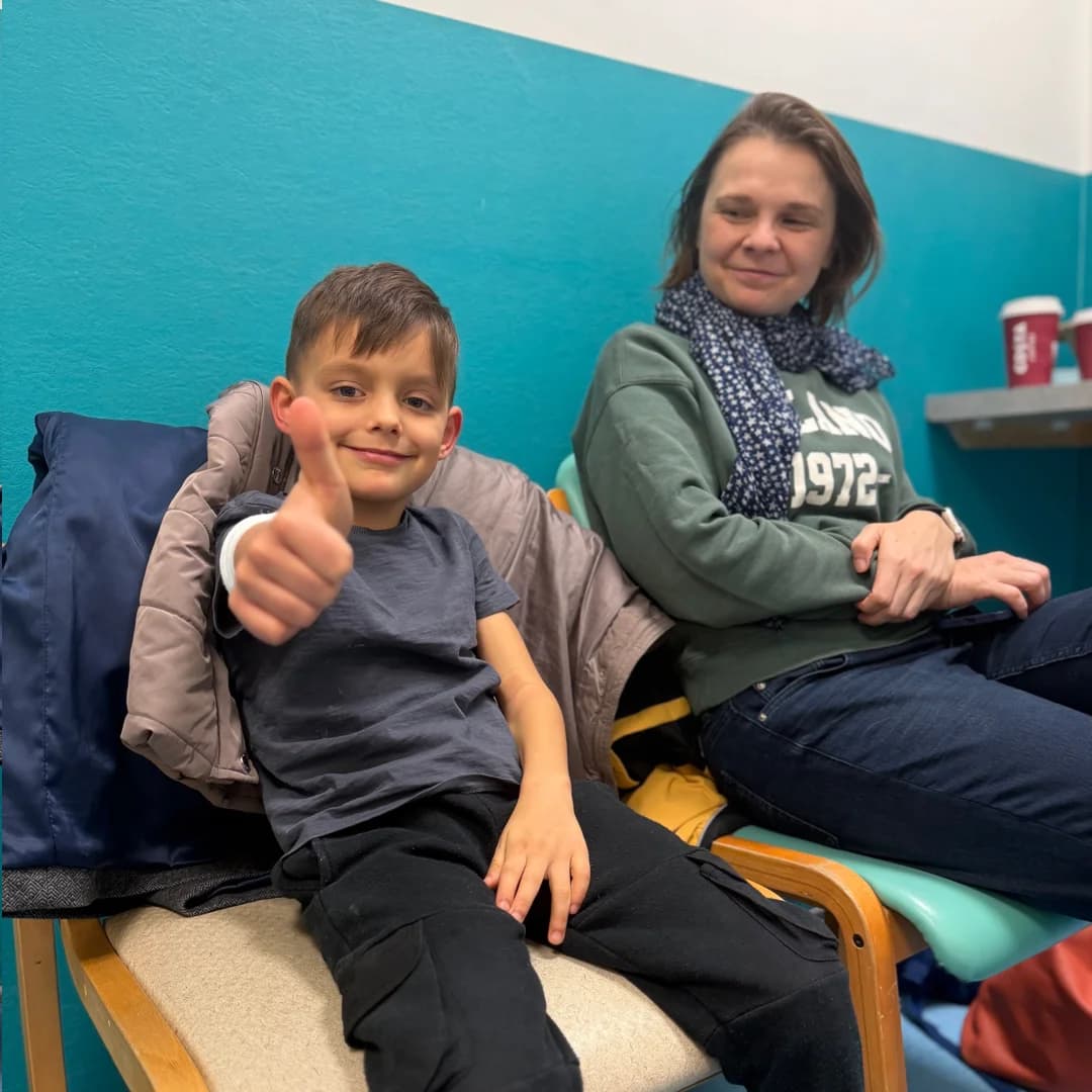 Aleks giving a thumbs up with his mom during hospital visit, showing their positive spirit