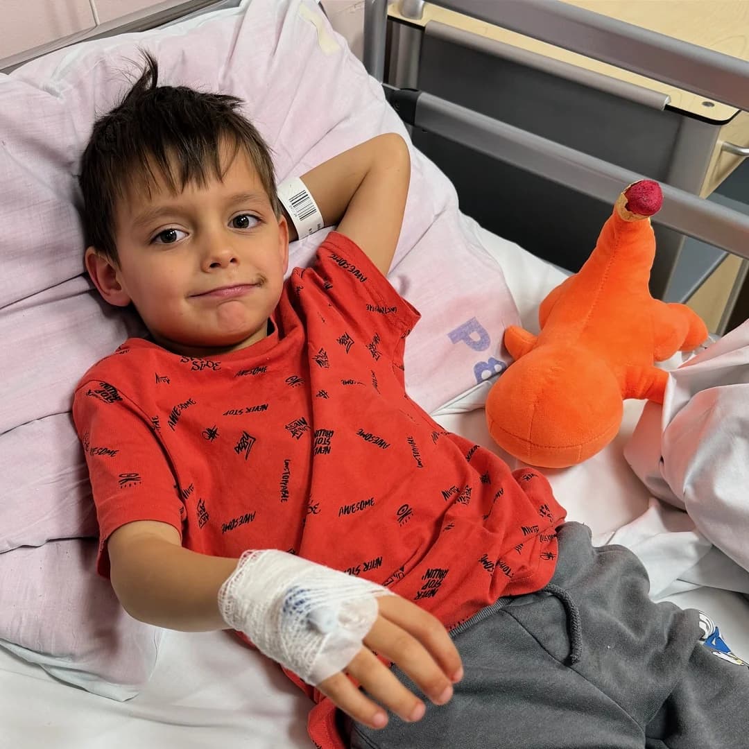 Aleks with his orange dinosaur toy in hospital bed, smiling through treatment